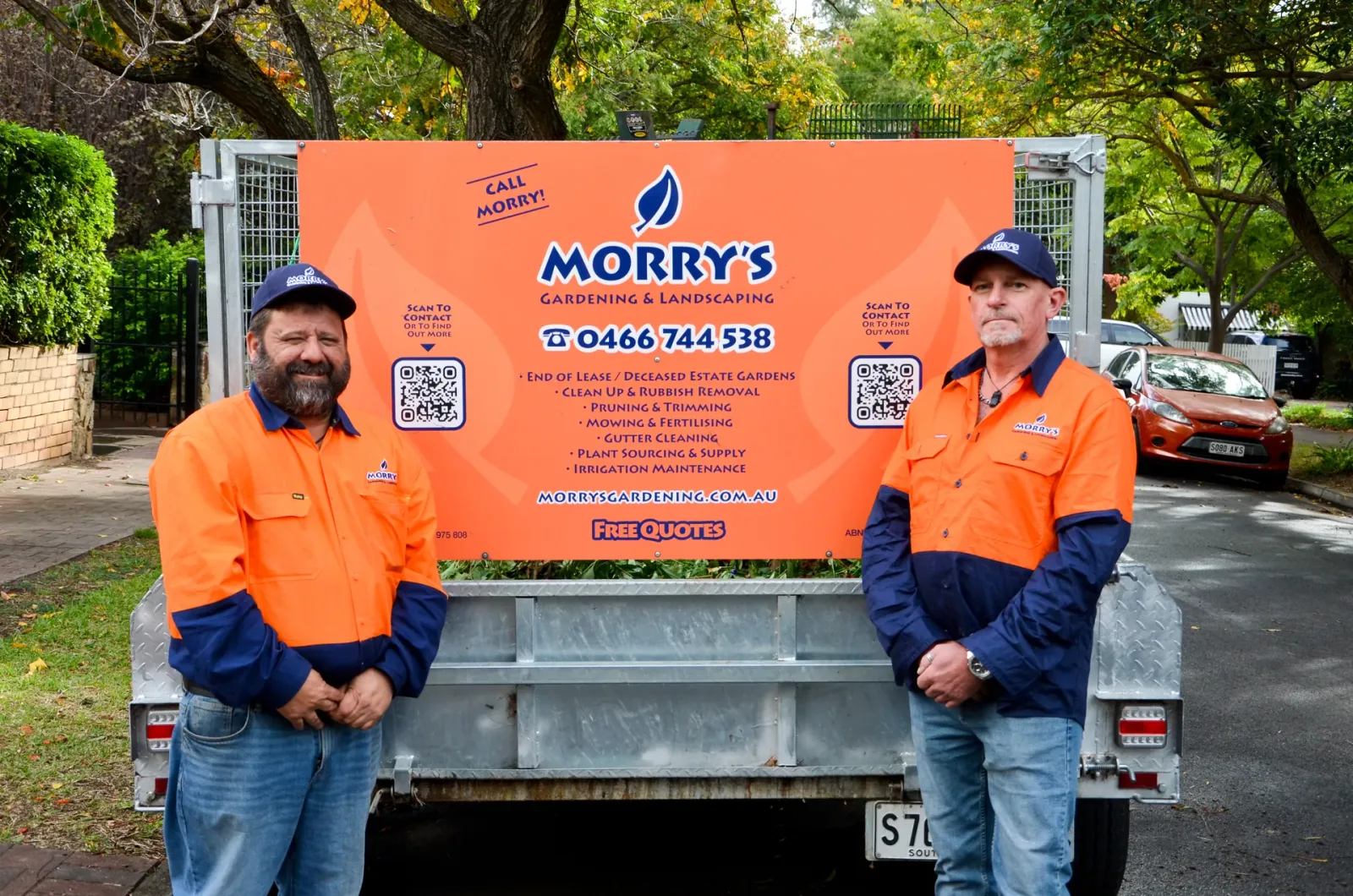 Two of Morry's crew in orange and navy workwear standing either side of the orange Morry's trailer